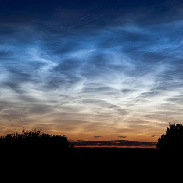 Wispy noctilucent clouds glow high above the silhouetted landscape
