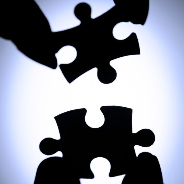 Silhouetted fingers push two matching puzzle pieces together, symbolizing teamwork